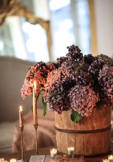 A Wooden Bucket With Purple And Rust-Colored Faux Blooms Plus Elegant Gold Candles Are A Stylish Combo For The Fall