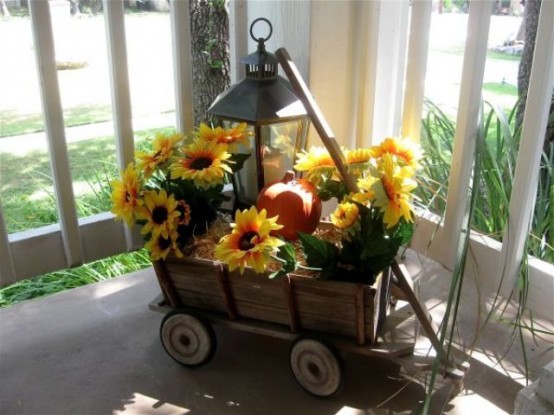 A Rustic Arrangement Of A Wooden Cart, Hay, A Faux Pumpkin And Sunflowers, A Candle Lantern Is A Stylish Outdoor Decoration