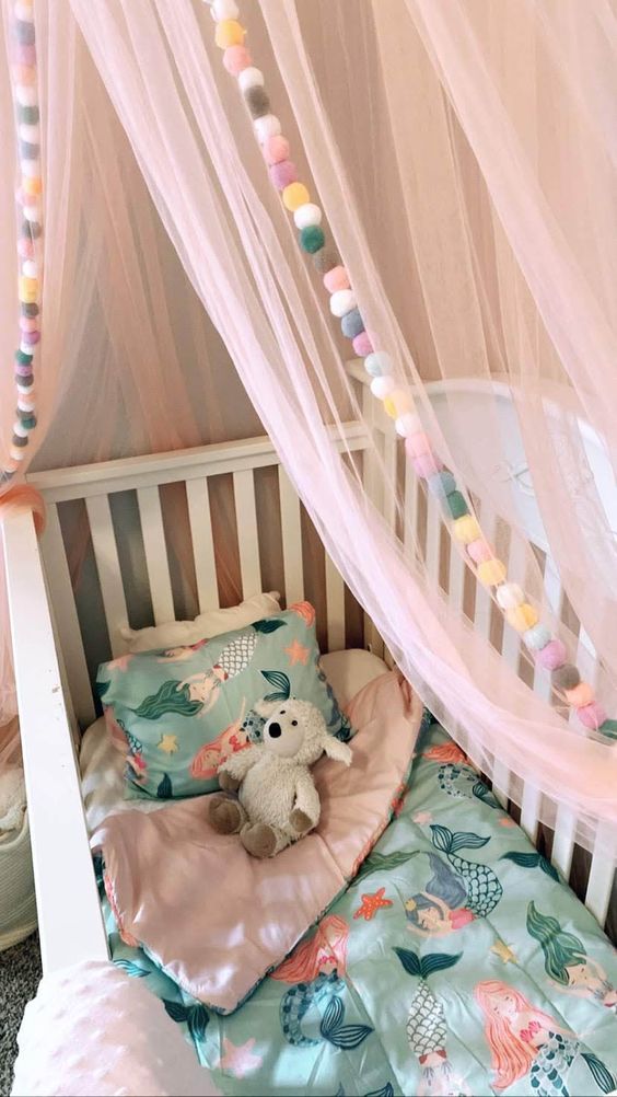 colorful pompom garlands and a light canopy to accent a baby's crib and make it cozier and welcoming
