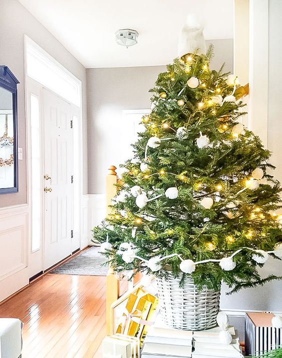 a Christmas tree with lights and white pompoms in a basket is a stylish piece for holiday decorating