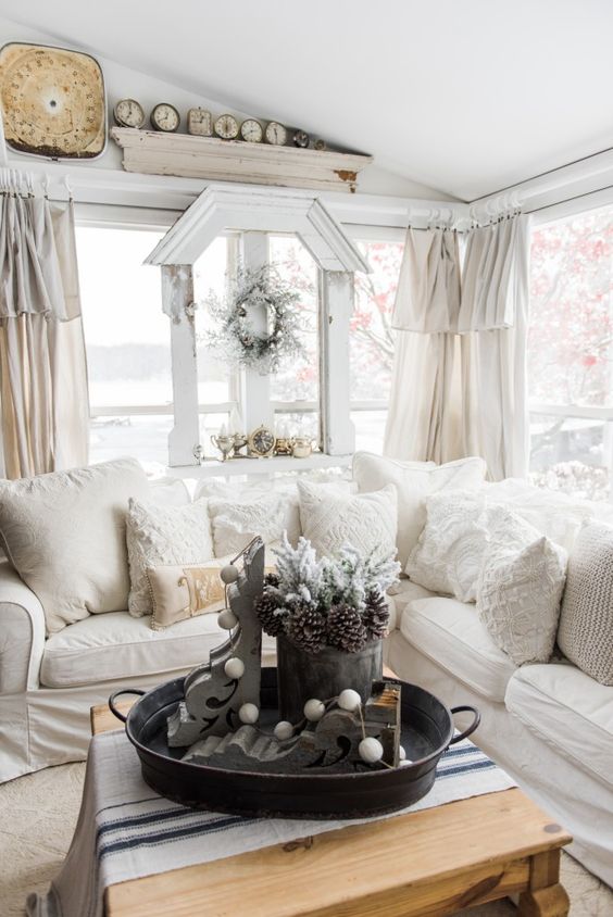 A Welcoming Neutral Farmhouse Sunroom With A Sectional, Vintage Decor, Wreaths, Clocks And Textiles In Creamy Shades