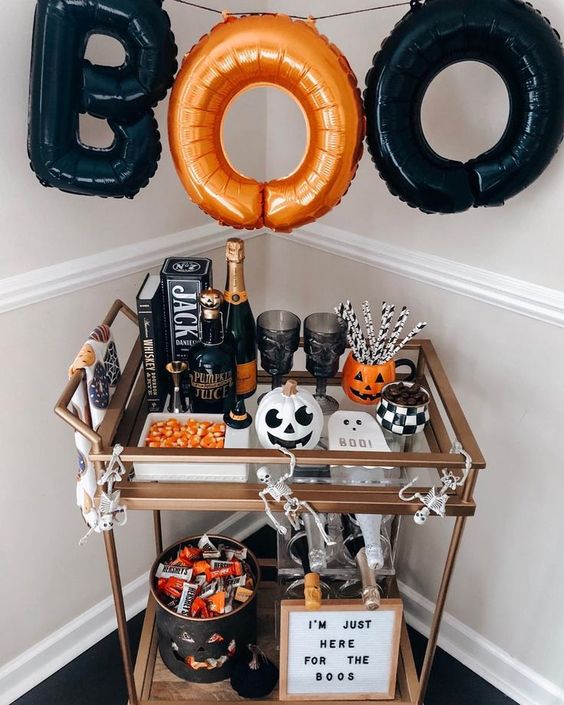 a bold Halloween bar cart with an orange and black letter garland, pumpkins, candies, an artwork and skeletons
