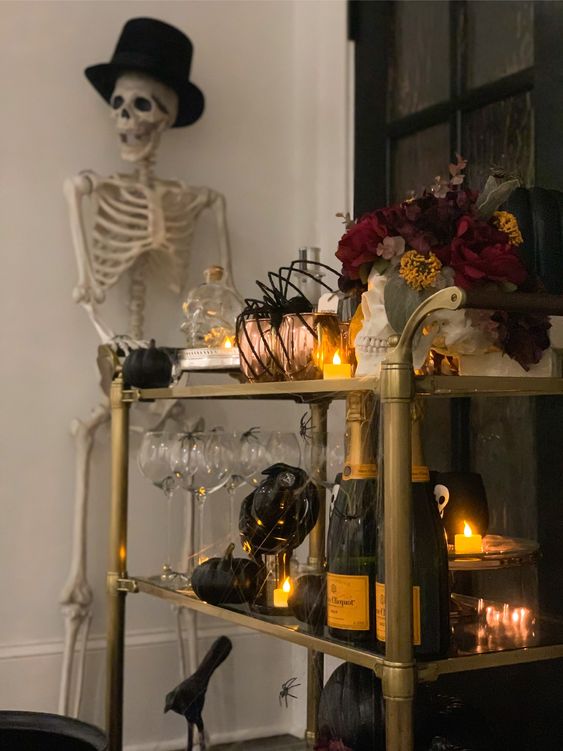 a haunted Halloween bar cart with candles, black pumpkins, a dark floral arrangement, copper mugs and spiders held by a skeleton