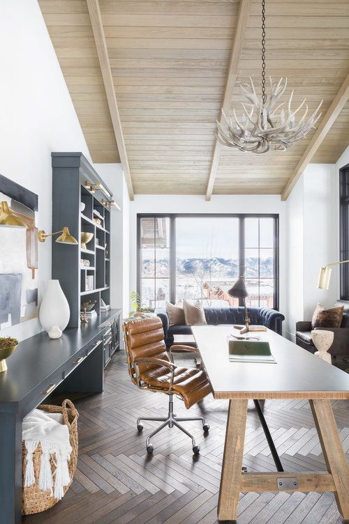 A Modern Rustic Home Office With A Large Graphite Grey Storage Unit, A Wooden Desk, A Leather Chair And An Antler Chandelier
