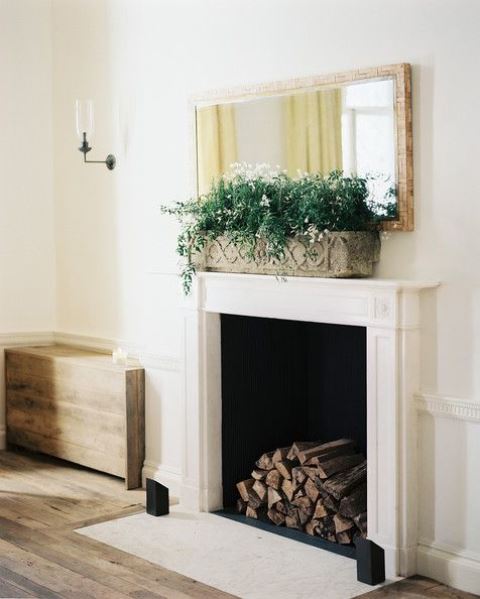 A Vintage And Refined Fireplace With A White Mantel And Firewood Inside Plus A Planter With Greenery And Blooms For A Chic Space