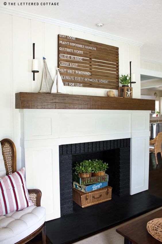 a coastal fireplace with a black and white surround, a stained mantel, a basket, boxes and potted greenery