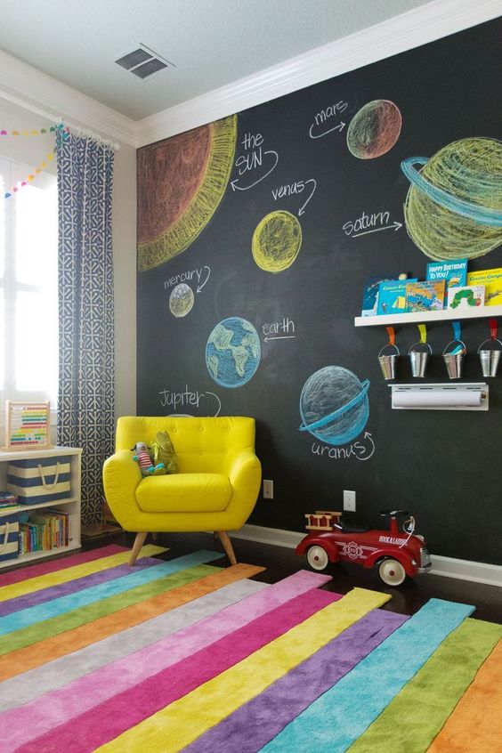 a colorful modern kids' playroom with a chalkboard wall, bold furniture and a rug, colorful crayons and books