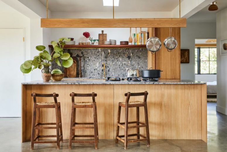 The Kitchen Is Done With Light-Colored Cabinets And Grey Terrazzo Surfaces Plus A Hanging Shelf Over The Kitchen