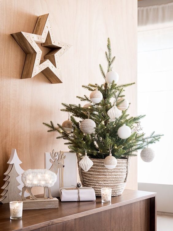 A Chic Tabletop Christmas Tree With Lights, Tan And White Oversized Ornaments Plus Wooden Decor Around For A Nordic Feel In The Space