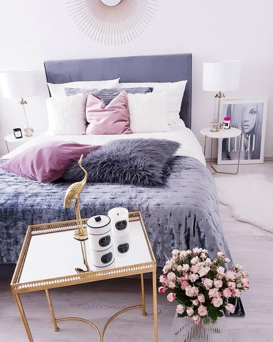 A Cool Feminine Bedroom With A Purple Bed, A Gold Nightstand With Candles, Pink Blooms, Pink, White And Purple Pillows