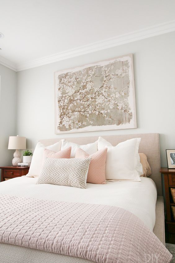 A Chic Feminine Bedroom With Grey Walls, An Upholstered Bed, Neutral And Pastel Bedding, Wooden Nightstands And A Floral Artwork