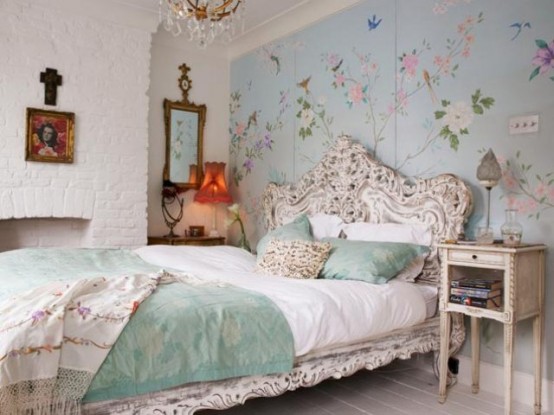 An Eclectic Feminine Bedroom With A Blue Floral Painted Wall, A White Carved Bed And Nightstands, A Faux Fireplace And Artworks Is Very Catchy